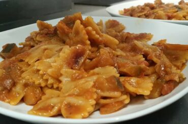 Italian man cooks farfalle pasta with eggplant and bacon