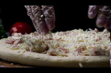 A female hands in cooking gloves sprinkling pizza with grated cheese, italian food concept. Frame