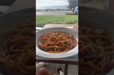 A Chinese person eating Italian food in a Greece cafe by the sea.