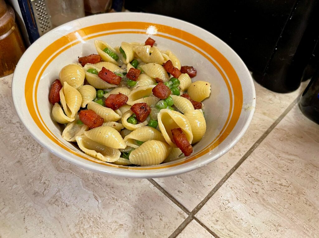 Pasta Shells with Onion and Peas Garnished with Guanciale in Parmesan Cheese sauce.