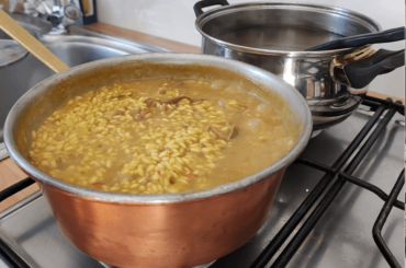 Risotto giallo con funghi porcini secchi; pentola di brodo fatto in casa sullo sfondo