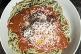 Meatball and red sauce on a bed of spinach fettuccine and topped with asiago