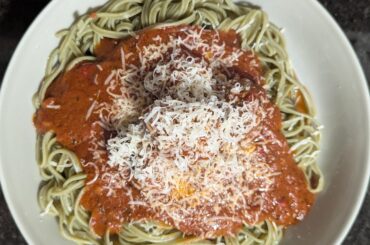 Meatball and red sauce on a bed of spinach fettuccine and topped with asiago