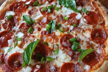 Homemade pizza 🍕 with provolone and wet mozzarella, topped with pepperoni, bacon sausage, green pepper, onion. Once out of the oven, basil leaves and drizzled with EVOO. 550° oven 8 minutes.