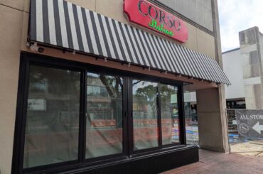 Front of a Corso Italian restaurant with a black-and-white striped awning and large glass windows beneath a red sign.
