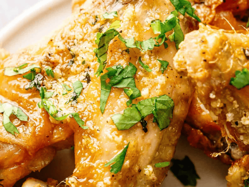 Close-up of seasoned baked chicken wings garnished with chopped fresh parsley on a white plate.