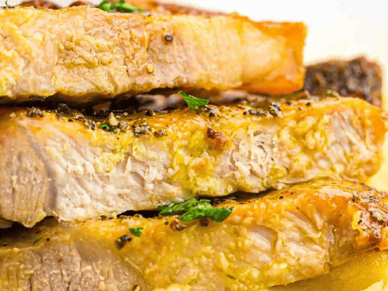 Close-up of three thick, cooked pork chops stacked on top of each other, seasoned with herbs and pepper.