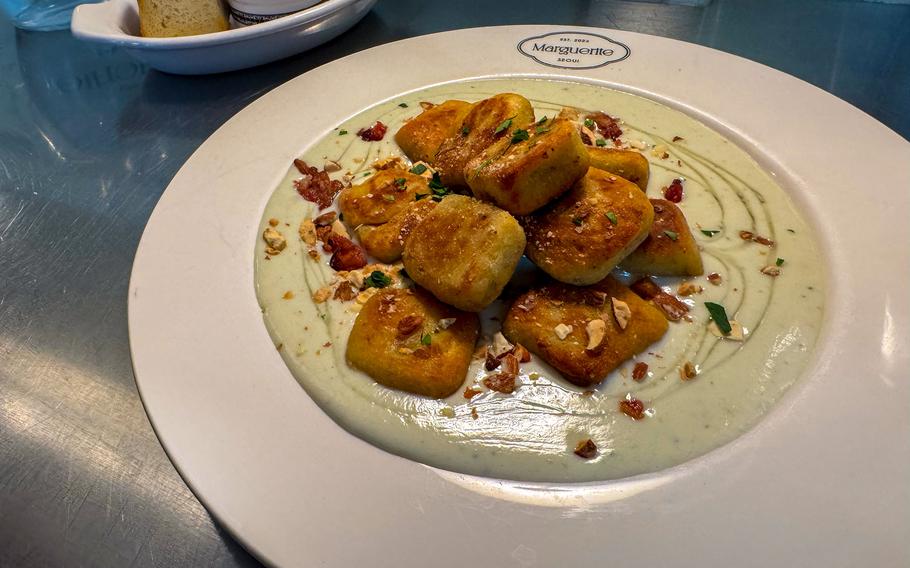 A close-up view of a white dinner plate, with gnocchi pasta piled on top of a pale green sauce.
