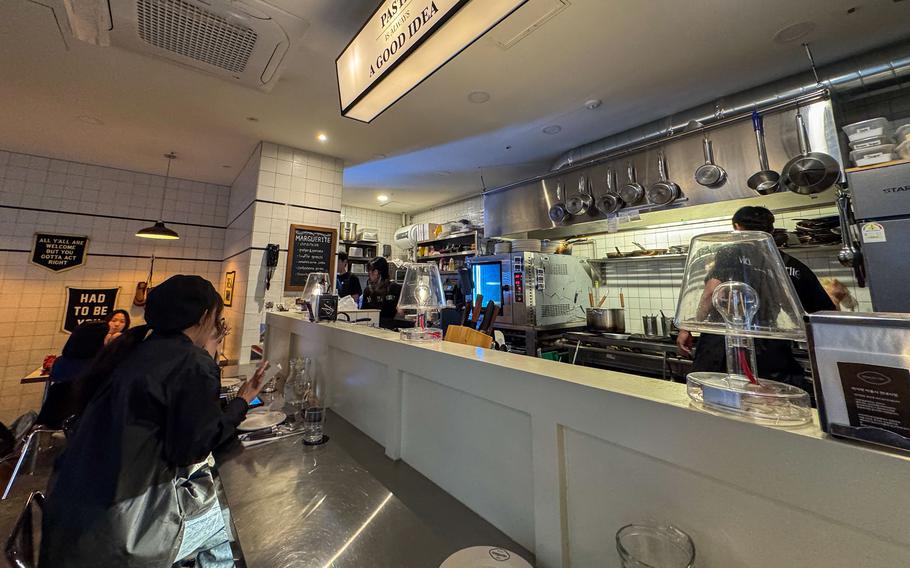 A restaurant kitchen is seen, with two South Korean employees working behind a small barrier and customers sitting at a counter on the other side.