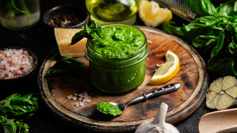 A jar of pesto on a cutting board surrounded by ingredients