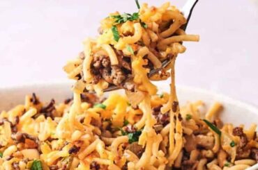 Fork lifting a serving of cheesy cheeseburger casserole garnished with parsley.