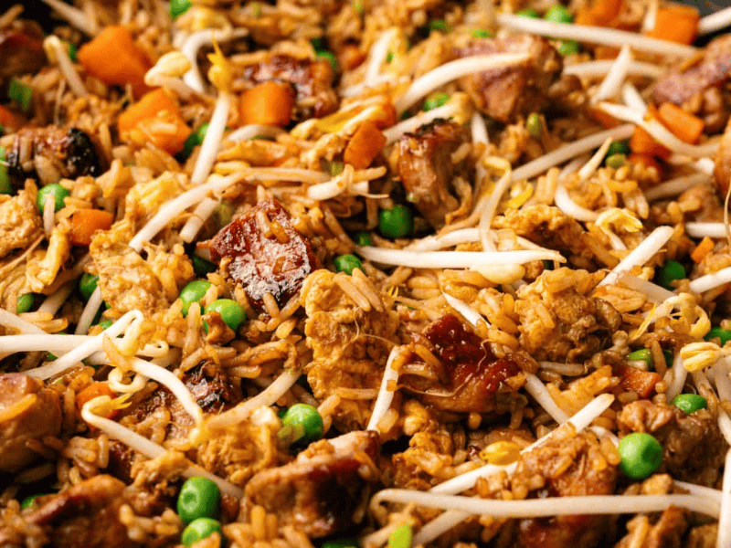 Close-up of fried rice with chunks of meat, peas, diced carrots, and bean sprouts mixed together.