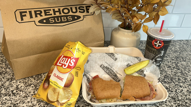 Firehouse Subs sandwich on kitchen counter with chips, bag, and drink